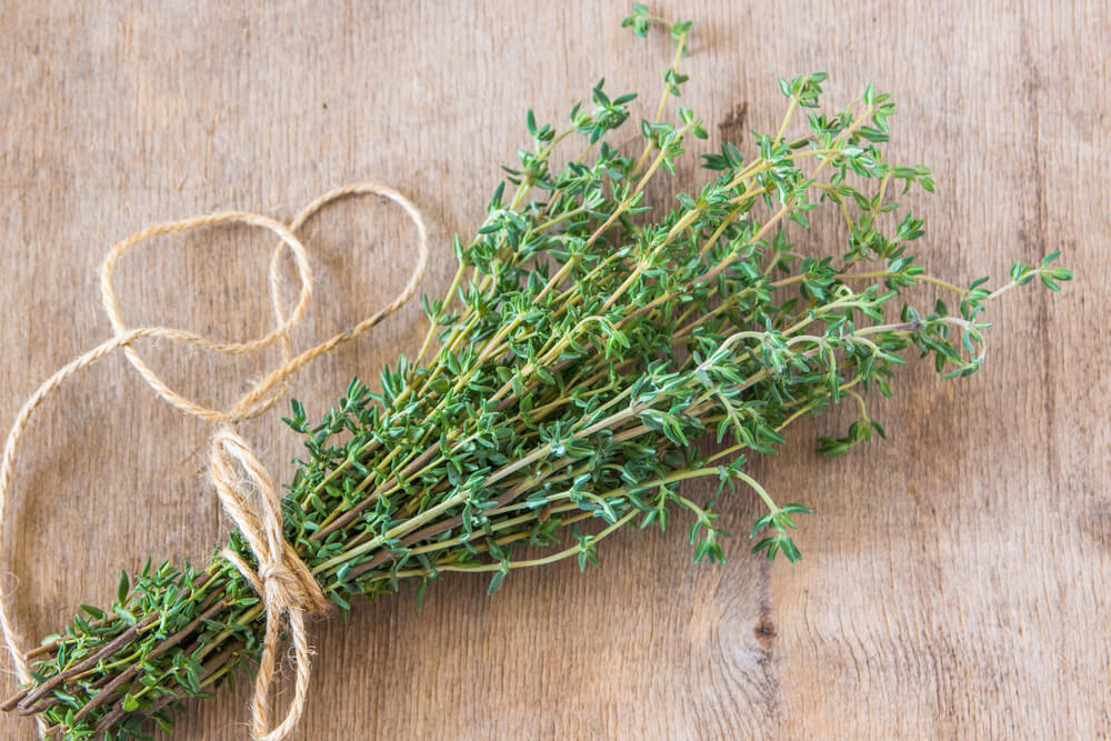 a bundle of fresh thyme tied together with cooking twine on a wooden cutting board