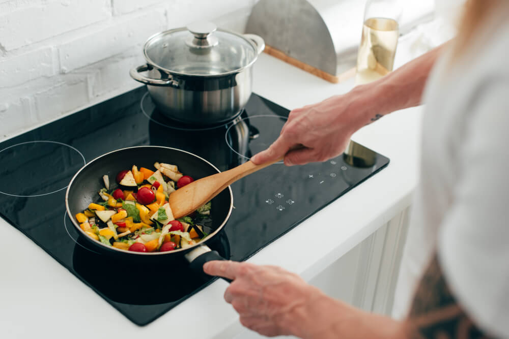 close up of a person's hands as they're sauteing vegetables with a wooden spatula on the stovetop