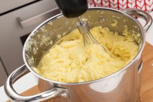 Someone mixes together the potatoes, sauteed ingredients, and egg in a pot.