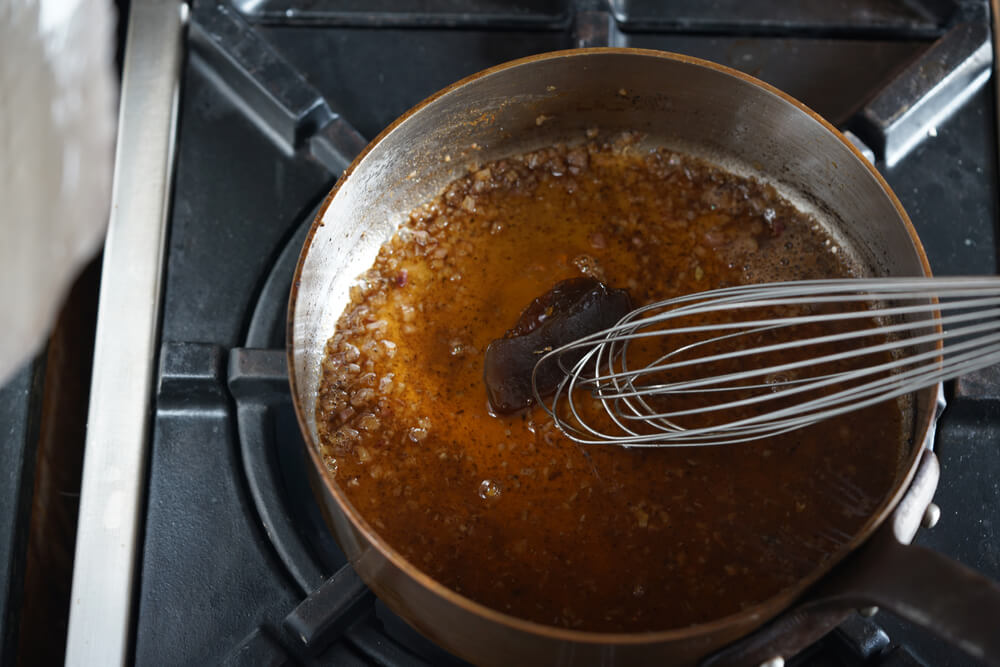 close up of a pan being deglazed with a metal whisk 