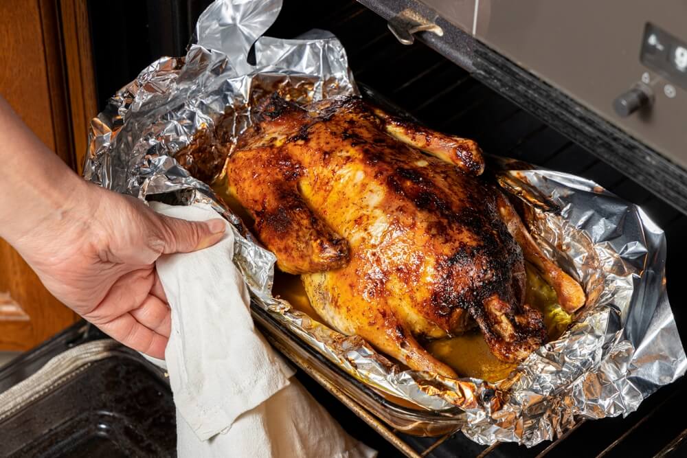 close up of a hand pulling a golden brown, roasted chicken out of the oven