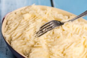 Someone transfers the potato filling into a casserole dish with a fork.